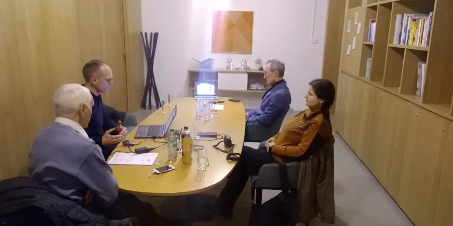 Wide view of a project meeting, four participants seated around an oval table with a projector screen at the far end.