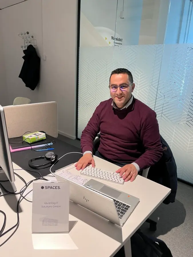 A Quantag engineer working at a desk in the company Munich office, the QuanTag IT Solutions GmbH nameplate on the table.