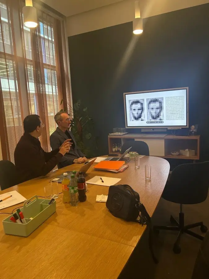 Meeting room discussion in front of a wall screen showing pixelated satellite imagery under analysis.